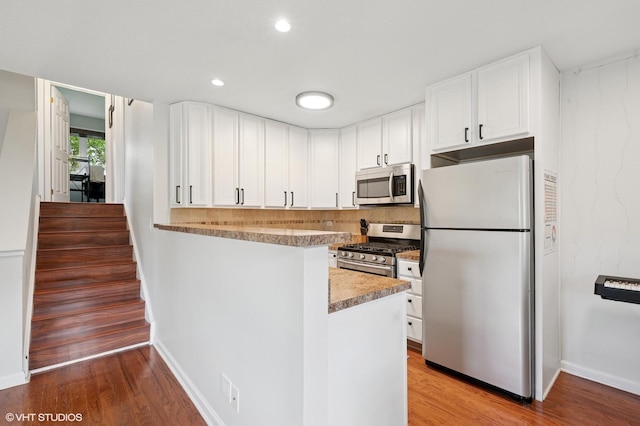 kitchen with stainless steel appliances, light wood finished floors, white cabinets, baseboards, and a peninsula