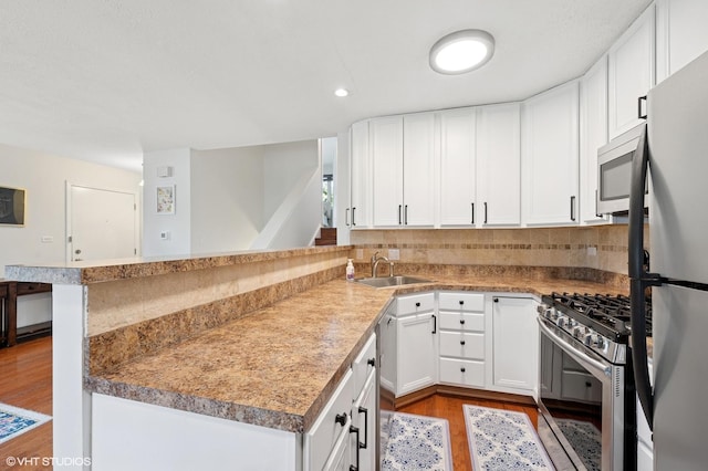 kitchen with stainless steel appliances, a sink, wood finished floors, a peninsula, and white cabinetry