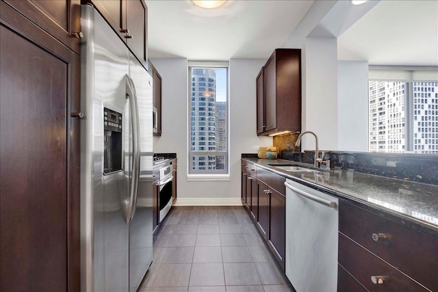 kitchen featuring stainless steel appliances, a sink, dark tile patterned floors, dark brown cabinetry, and baseboards