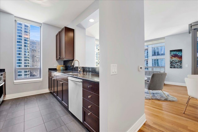 kitchen featuring stainless steel dishwasher, a sink, baseboards, dark countertops, and dark brown cabinets