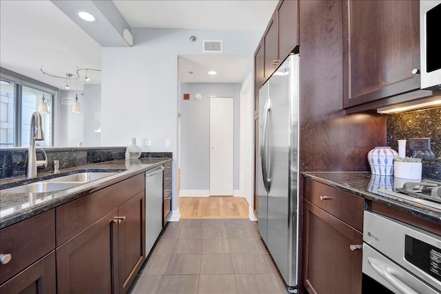 kitchen with stainless steel appliances, a sink, dark stone countertops, tile patterned floors, and backsplash