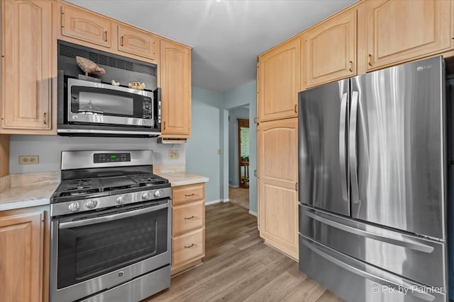 kitchen with stainless steel appliances, light brown cabinetry, light countertops, light wood-style floors, and baseboards