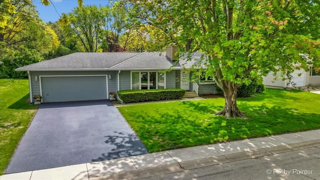 view of front of home with a garage, asphalt driveway, a chimney, and a front lawn