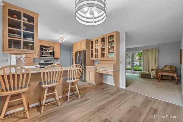 kitchen with stainless steel appliances, light brown cabinetry, light wood-style flooring, glass insert cabinets, and a sink