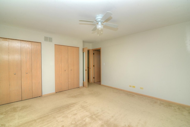 unfurnished bedroom featuring multiple closets, light carpet, and baseboards