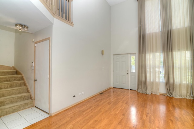 entryway featuring a high ceiling, stairway, light wood-style floors, and baseboards