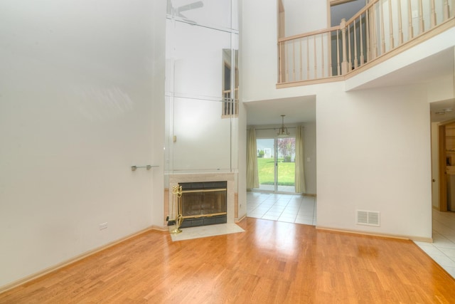 unfurnished living room with a towering ceiling, wood finished floors, a fireplace with flush hearth, and baseboards