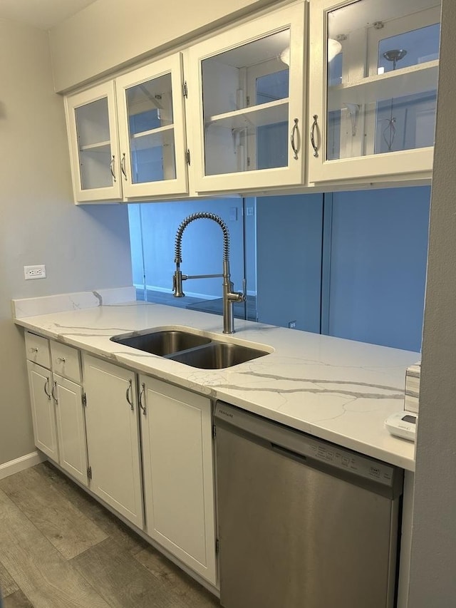 kitchen featuring stainless steel dishwasher, a sink, white cabinetry, dark wood-type flooring, and light stone counters