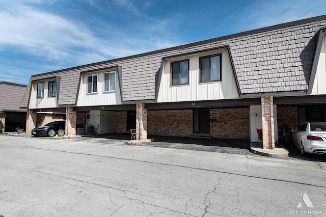 view of side of property featuring brick siding, mansard roof, and cooling unit
