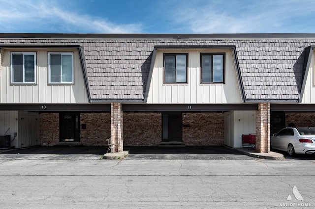 view of side of home featuring brick siding, mansard roof, central air condition unit, and covered parking