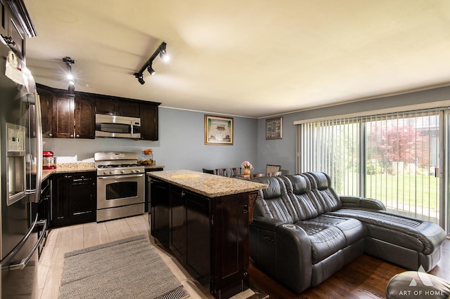 kitchen with stainless steel appliances, open floor plan, rail lighting, light wood finished floors, and light stone countertops