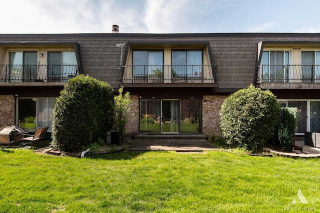 back of property with brick siding, mansard roof, a balcony, and a lawn