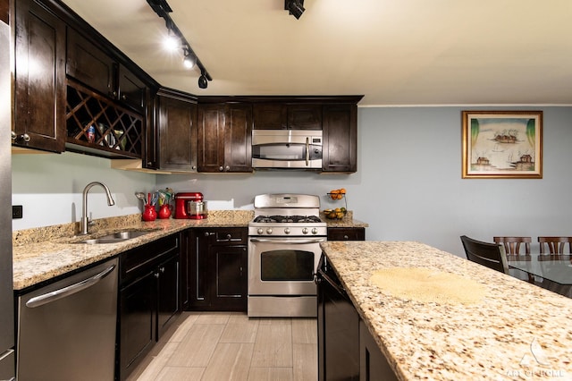 kitchen featuring appliances with stainless steel finishes, a sink, light stone countertops, dark brown cabinets, and light wood-style floors