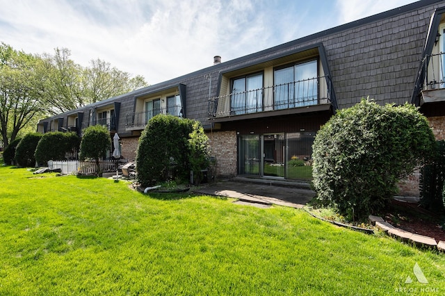 rear view of property featuring mansard roof, brick siding, a yard, and a balcony