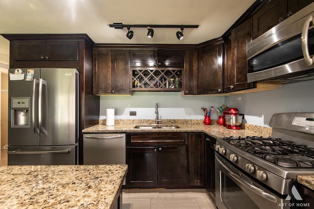 kitchen with appliances with stainless steel finishes, a sink, dark brown cabinetry, light stone counters, and rail lighting