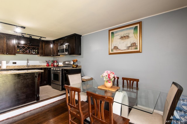 dining room with bar with sink, baseboards, track lighting, and light wood-type flooring