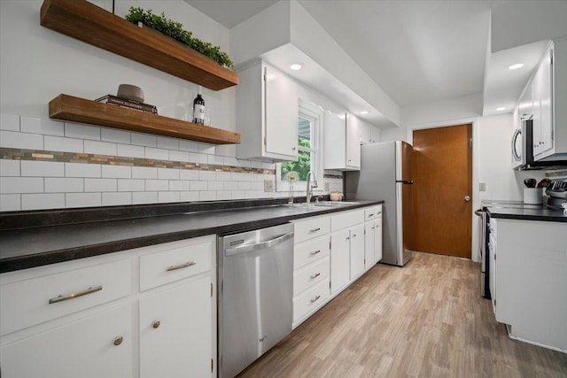 kitchen with stainless steel appliances, a sink, dark countertops, light wood finished floors, and white cabinets