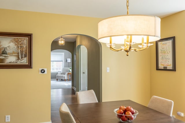 dining room featuring arched walkways, wood finished floors, a chandelier, and baseboards