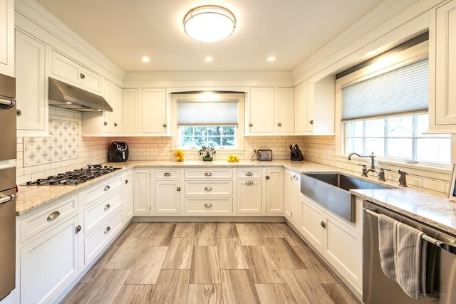kitchen featuring stainless steel appliances, a sink, under cabinet range hood, white cabinets, and recessed lighting