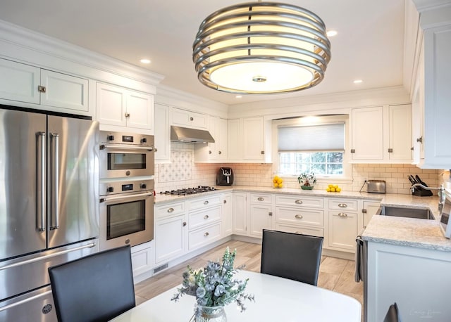 kitchen with stainless steel appliances, under cabinet range hood, white cabinetry, tasteful backsplash, and crown molding
