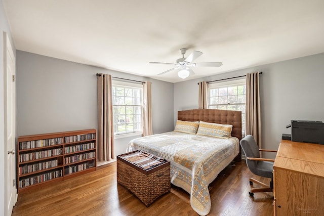 bedroom with multiple windows, wood finished floors, ceiling fan, and a desk