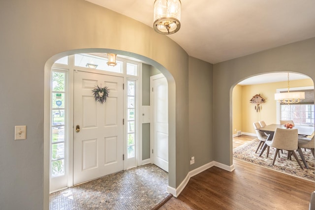 entryway featuring arched walkways, a chandelier, wood finished floors, and plenty of natural light