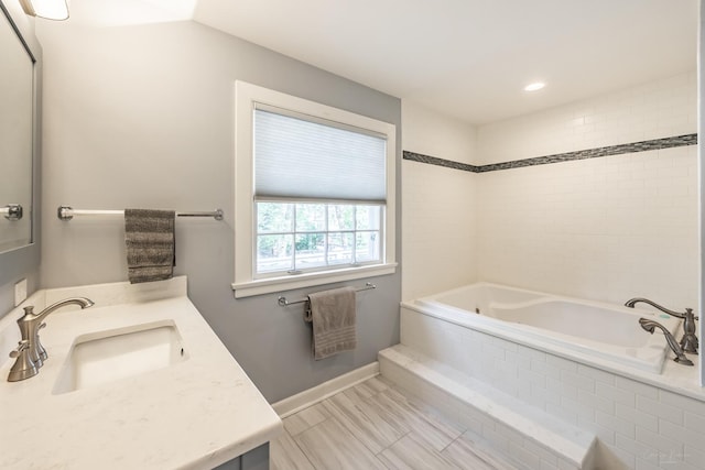 full bath featuring a relaxing tiled tub, baseboards, and vanity