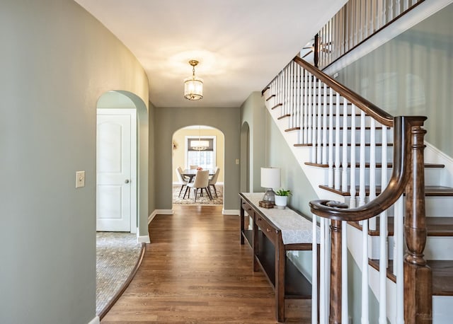 foyer entrance featuring arched walkways, wood finished floors, stairway, baseboards, and a chandelier