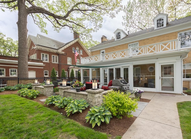 rear view of house with a balcony, brick siding, a patio area, fence, and french doors