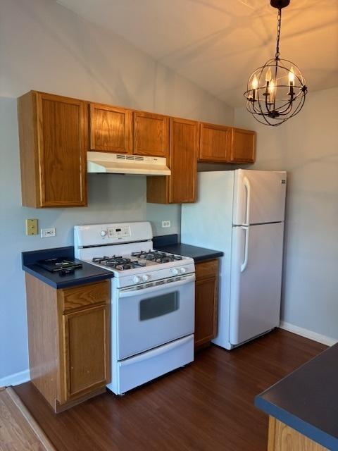 1286 N Red Oak Cir Unit 4, Round Lake Beach, IL 60073 - kitchen featuring white appliances, under cabinet range hood, dark wood-style floors, brown cabinets, and a chandelier