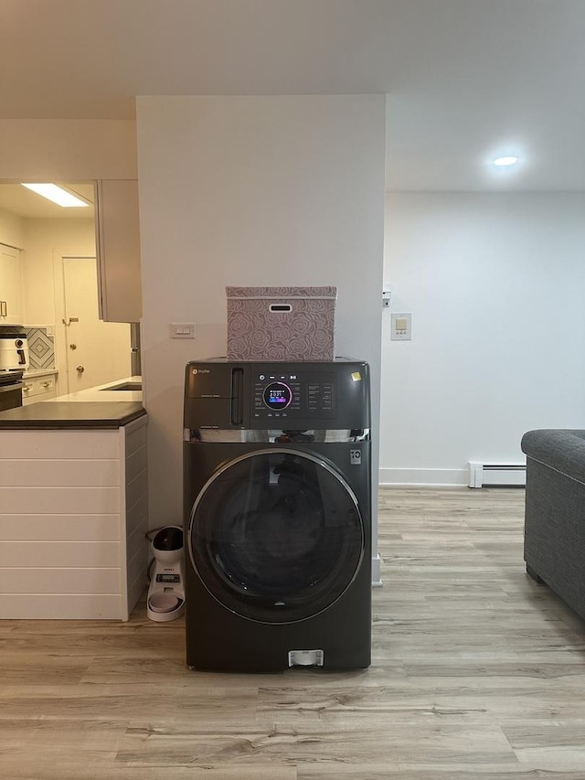 clothes washing area featuring washer / dryer, a baseboard heating unit, and light wood-style floors