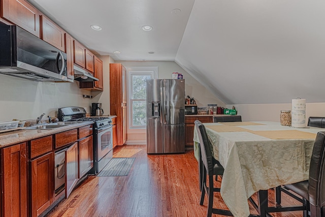 kitchen featuring stainless steel appliances, under cabinet range hood, a sink, light wood-type flooring, and lofted ceiling