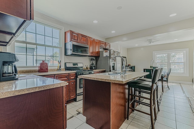 kitchen with appliances with stainless steel finishes, a sink, light tile patterned floors, a breakfast bar area, and light countertops