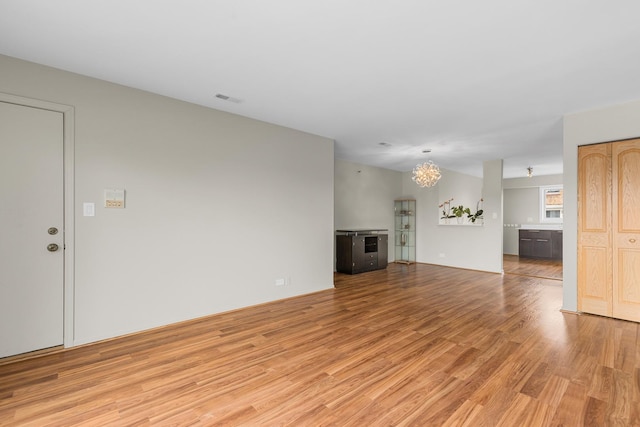 unfurnished living room with light wood-type flooring and a chandelier