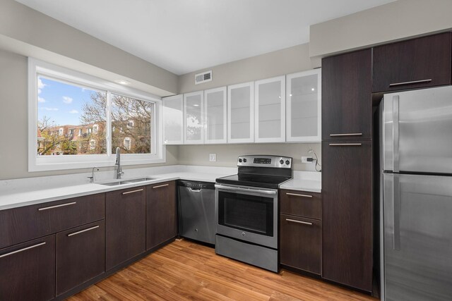 kitchen with stainless steel appliances, a sink, light countertops, glass insert cabinets, and dark brown cabinetry