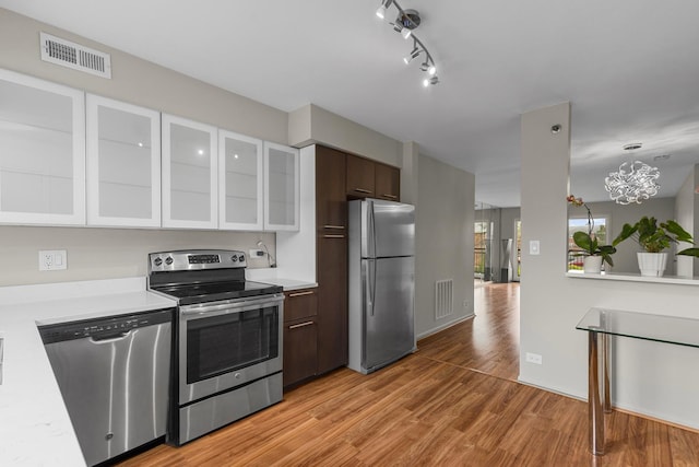 kitchen featuring appliances with stainless steel finishes, light countertops, light wood-style flooring, glass insert cabinets, and white cabinets