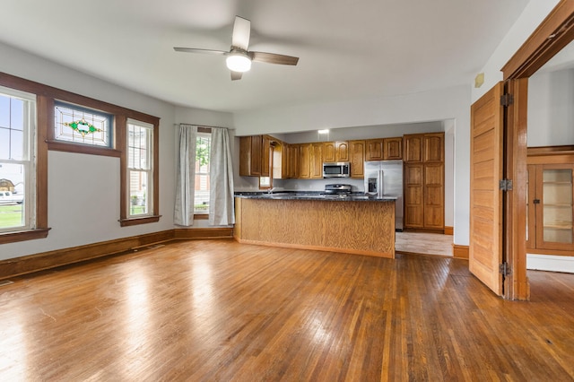 201 E Court St, Paris, IL 61944 - kitchen featuring appliances with stainless steel finishes, brown cabinetry, dark countertops, dark wood-style floors, and a peninsula