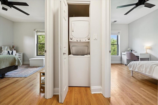 bedroom with estacked washer and dryer, wood finished floors, multiple windows, and a ceiling fan