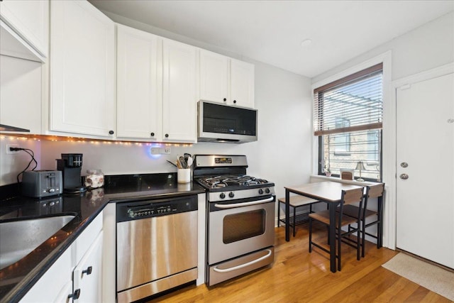 kitchen with stainless steel appliances, light wood-style floors, white cabinetry, dark stone counters, and a sink