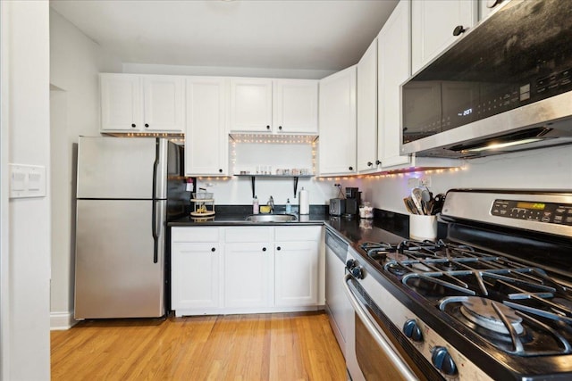 kitchen featuring appliances with stainless steel finishes, white cabinetry, light wood-style floors, dark countertops, and a sink