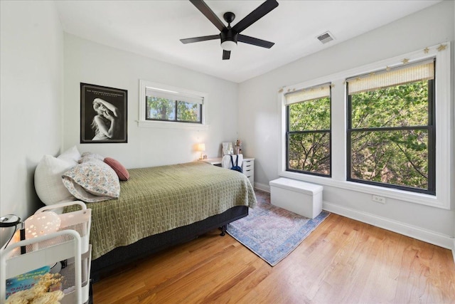 bedroom with multiple windows, baseboards, wood finished floors, and a ceiling fan
