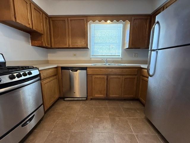 39 King Arthur Ct Unit 10, Northlake, IL 60164 - kitchen featuring appliances with stainless steel finishes, a sink, brown cabinetry, light countertops, and light tile patterned flooring