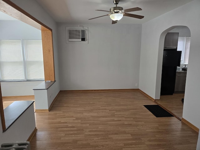 unfurnished dining area featuring a ceiling fan, arched walkways, a wall mounted air conditioner, wood finished floors, and baseboards