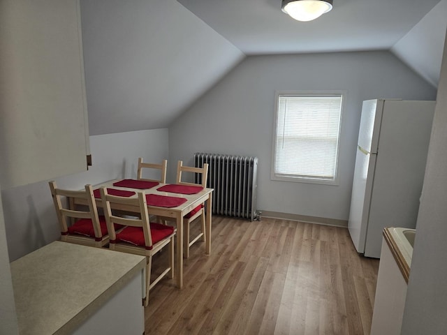 dining room featuring radiator, light wood-style flooring, and lofted ceiling