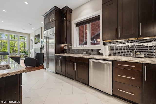 kitchen featuring stainless steel appliances, a sink, backsplash, light stone counters, and recessed lighting