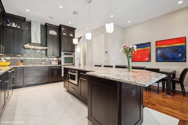 kitchen with wall chimney exhaust hood, decorative backsplash, glass insert cabinets, decorative light fixtures, and light tile patterned floors
