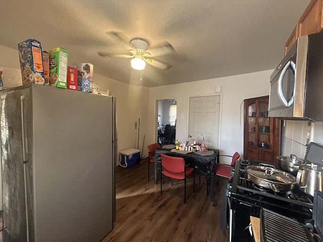 kitchen featuring freestanding refrigerator, stainless steel microwave, gas stove, dark wood-type flooring, and ceiling fan