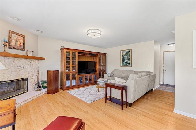 living area with light wood-style flooring, a stone fireplace, and baseboards