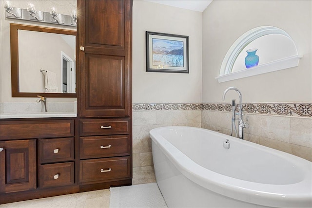 bathroom with a freestanding tub, vanity, tile walls, and a wainscoted wall