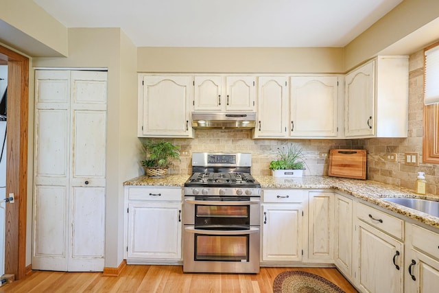 43 Mohawk St, Cary, IL 60013 - kitchen featuring range with two ovens, under cabinet range hood, light stone countertops, light wood-style floors, and backsplash